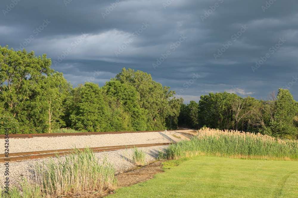 Dark gray storm cloudsmoving out with bright sun shining on railroad tracks in Lakevile, New York