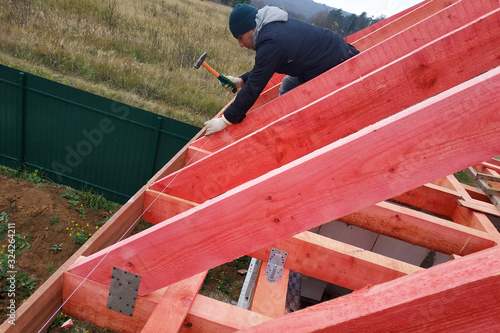 A man fastens two wooden beams with a self-tapping screw, installing wooden rafters on the roof.