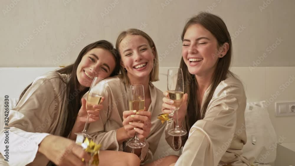 Cheerful rejoicing young girls friends are throwing out the confetti on the bed in the light bedroom Cheerful rejoicing young girls friends are throwing out the confetti on the bed in the light bedroom