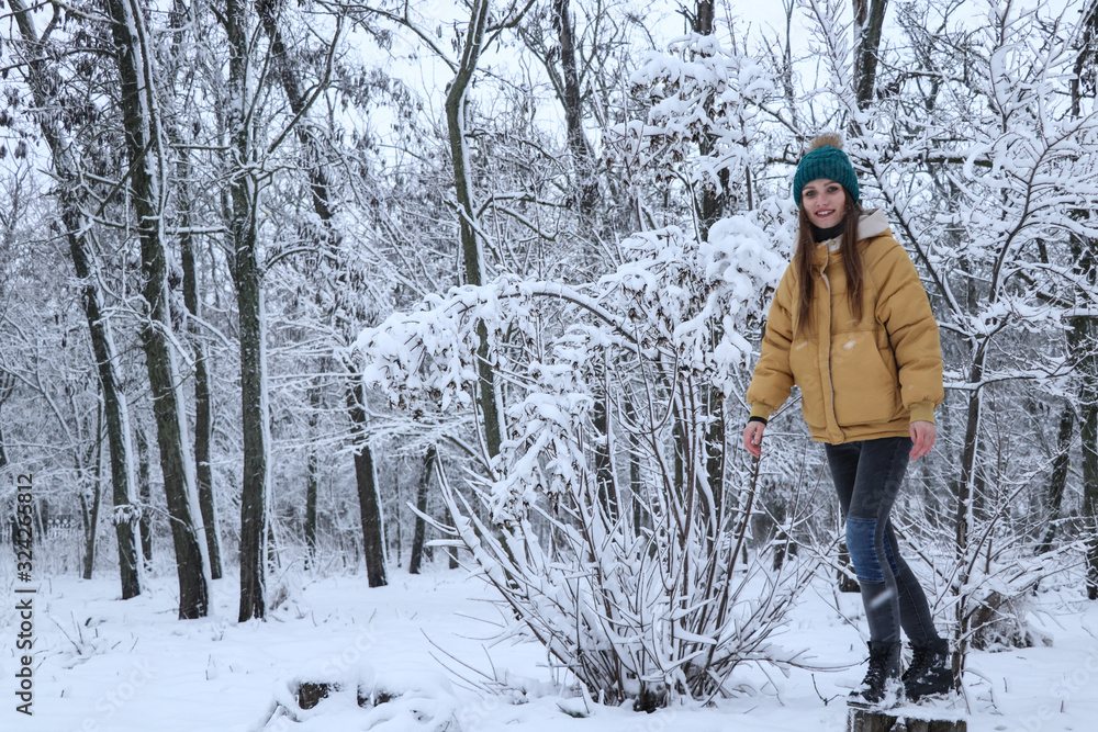 Beautiful girl in a yellow jacket, jeans and a green hat on the snow. Snowy weather, everything in the snow is white. Snowflakes.