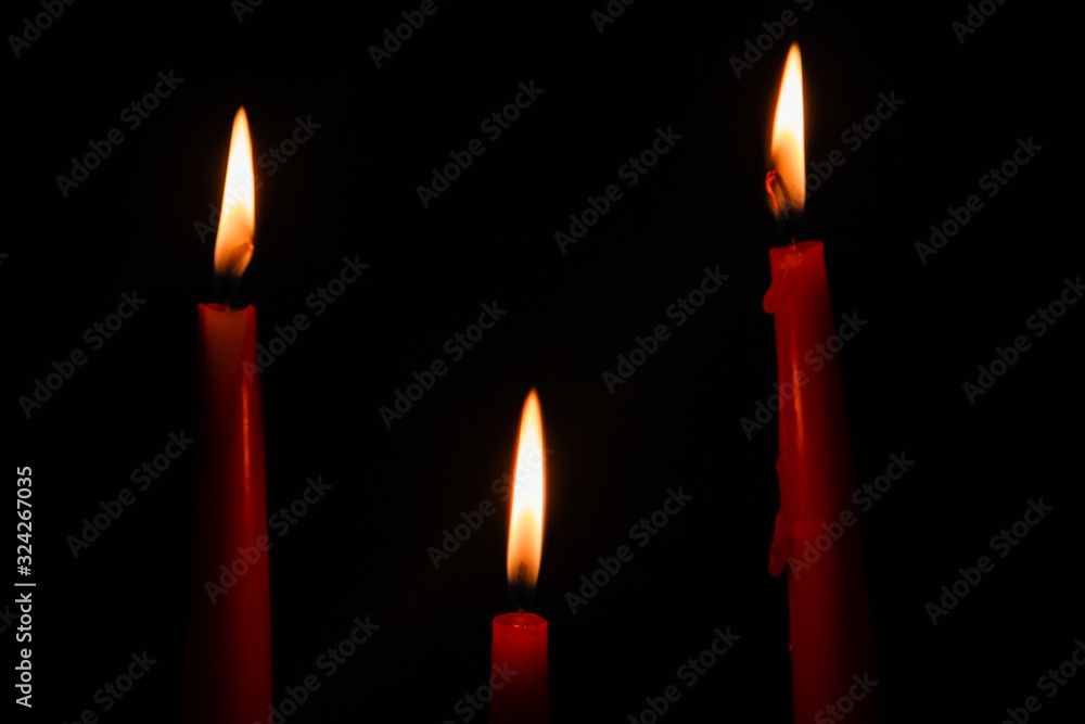 Three red candles on a black background in the dark. Three red candles on a black background in the dark.
