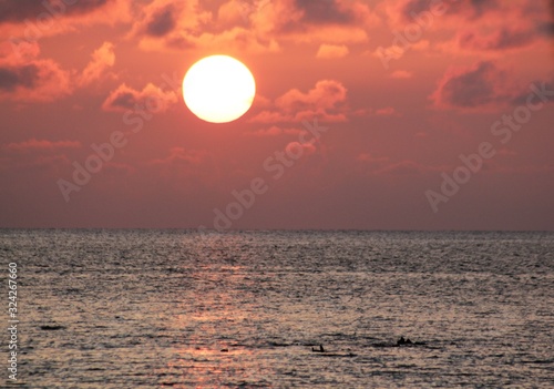 Fototapeta Naklejka Na Ścianę i Meble -  A full round sun beginning to set above the ocean