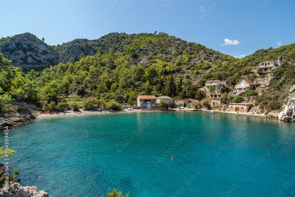 During a sunny summer day view of a beautiful small quiet cove with a pebble beach and turquoise blue water, green vegetation covered hill in the background, Mala Stiniva beach, Hvar Island, Croatia.