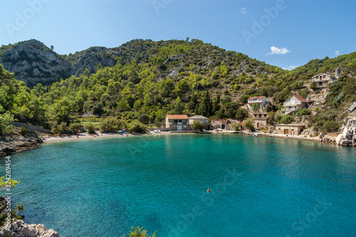 During a sunny summer day view of a beautiful small quiet cove with a pebble beach and turquoise blue water, green vegetation covered hill in the background, Mala Stiniva beach, Hvar Island, Croatia. photo