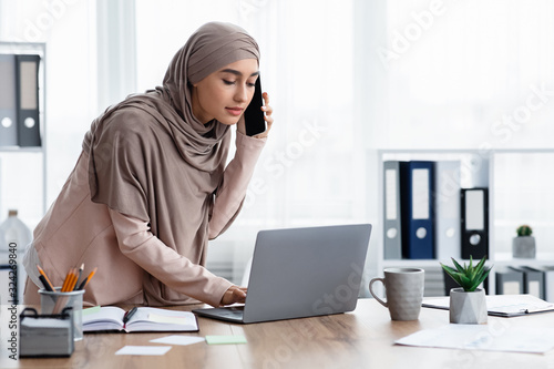 Busy arabic businesswoman using laptop and talking on cellphone, consulting client