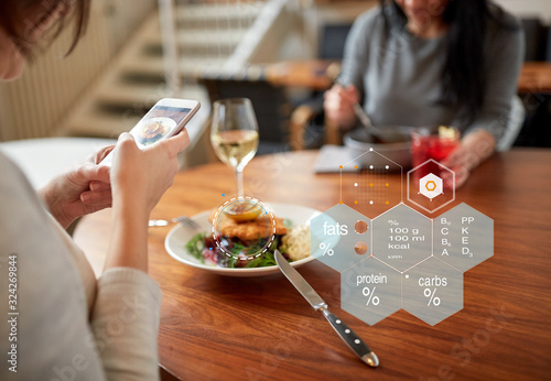 new nordic cuisine, technology and people concept - woman with food on smartphone screen and nutritional value chart r at restaurant photo