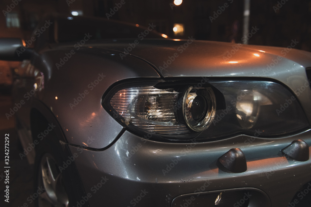 Grey car with broken headlight after a crash accident. Car on the street at night. Side view. Closeup.