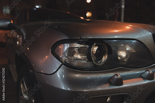 Grey car with broken headlight after a crash accident. Car on the street at night. Side view. Closeup. © Alexander