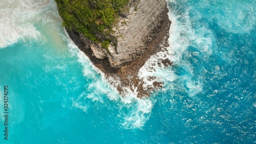 White-blue waves beat on the rocks of the island of Nusa Penida near Kelingking beach.