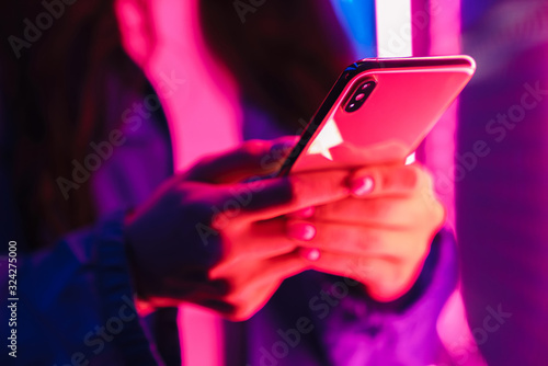 Woman posing over neon lights using mobile phone.