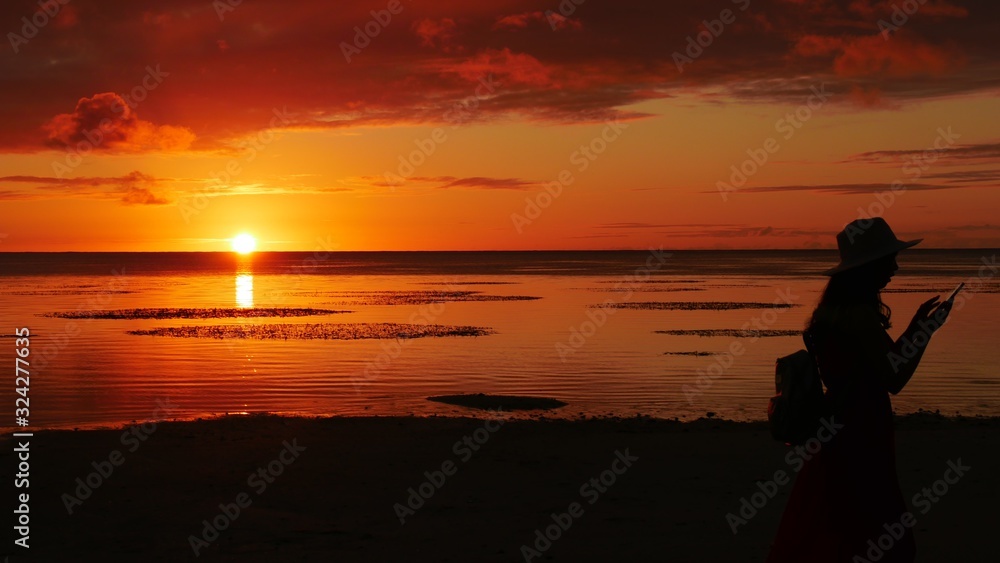 Fiery sunset in the sea with the silhouette of a woman taking photos with her phone