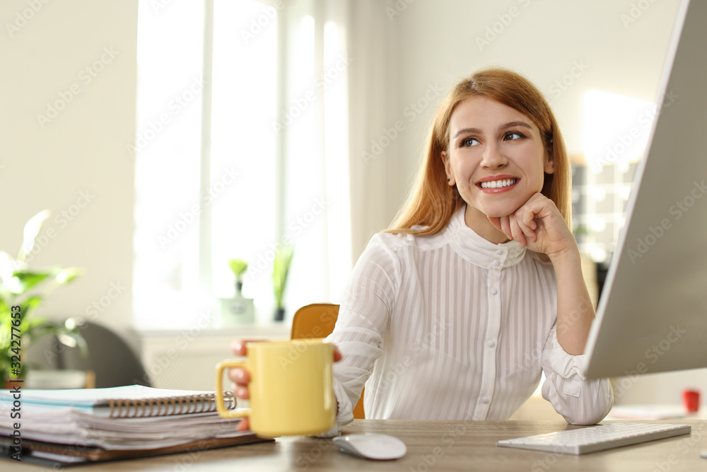 Young woman with cup of drink relaxing at table in office during break Young woman with cup of drink relaxing at table in office during break