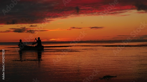 Wide shot with the silhouette of two boaters in the sea with dramatic sunset background