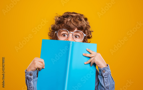 Funny schoolboy hiding behind textbook photo