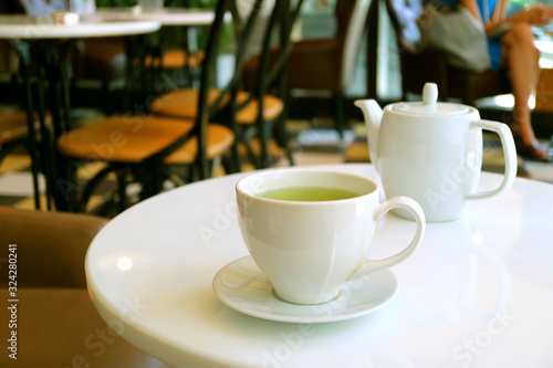 Closeup a cup of green tea and teapot on white round table in a tearoom