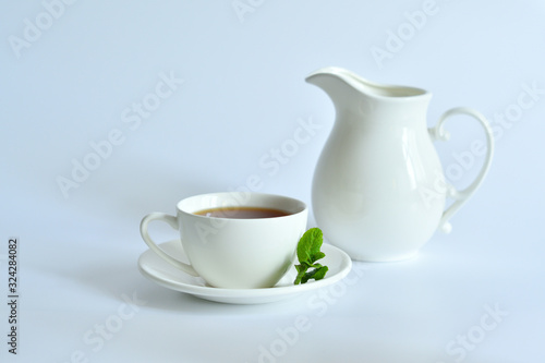 One small cup of tea with mint and jug on white background.