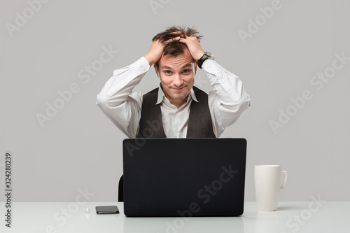 Businessman in a white t-shirt and grey vest is shocked checking information on a laptop