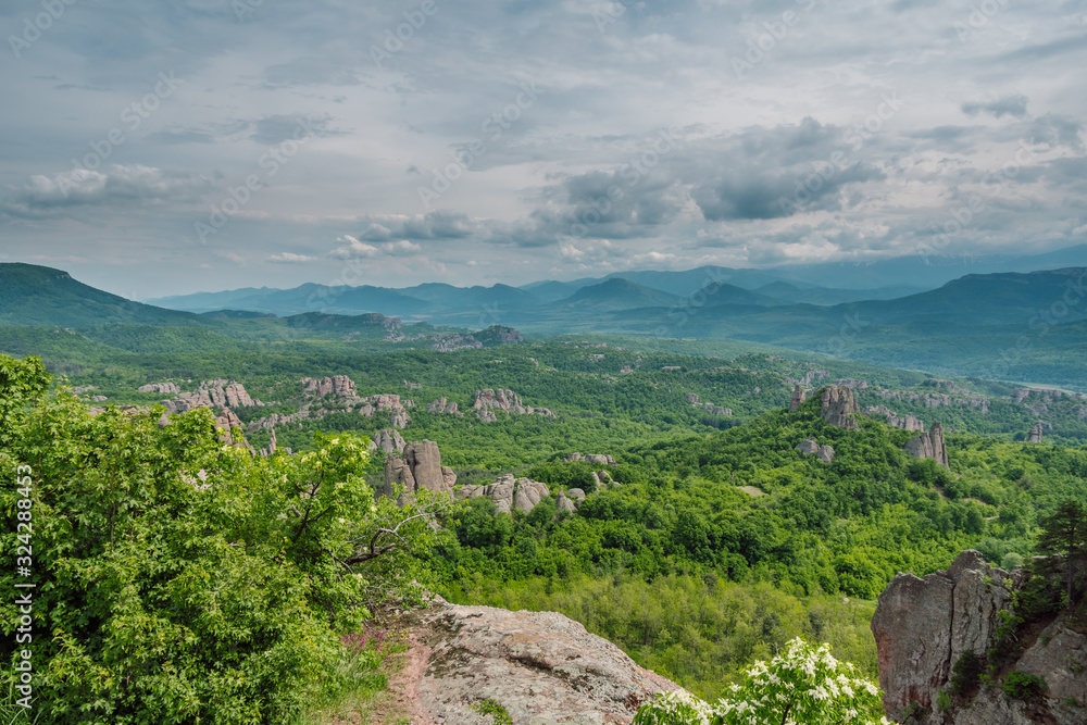 Green mountain valley and rock formations, dramatic cloudy sky in the background. Belogradchik Rocks in Bulgaria,  Northwest  Balkan Mountain (Stara Planina), Europe. 