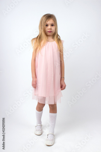 little blonde girl of six seven years with long hair in a light pale pink dress, white golf and white shoes on a white background
