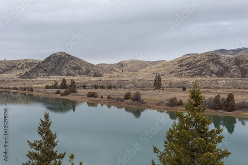 Two trees in foreground with calm green river and rolling hills © Richard