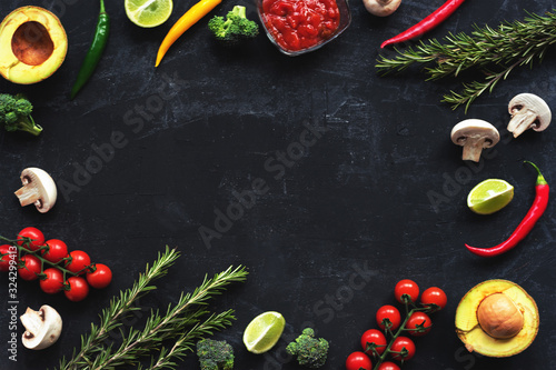 Ingredients for Italian cuisine: tomatoes, mushrooms, broccoli, chilli peppers, avocado, rosemary, lime and red sauce on a black background. Top view, flat lay, copy space.