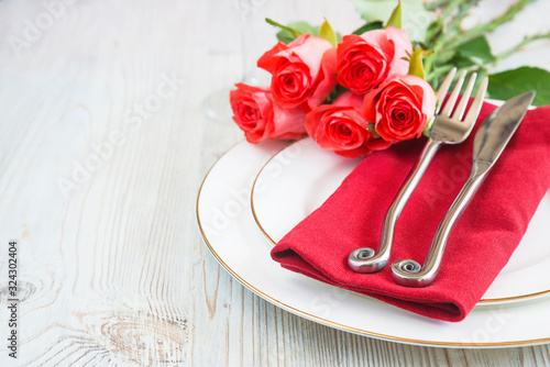 Romantic table setting. Forged fork and knife on red napkin and white plates and bouquet of red roses. Close up, selective focus