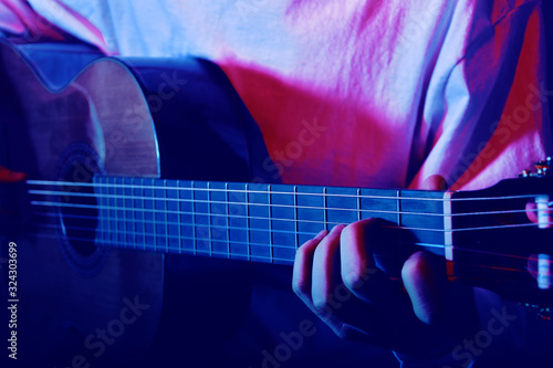 Close-up of fingers on the neck of an acoustic guitar. Muchina plays the guitar in neon. Musician, music, training.