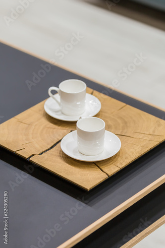 Modern wooden stand and two white coffee cups on a coffee table. Beautiful dishes on the table in detail