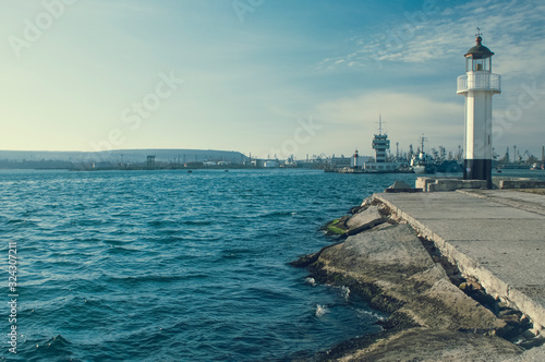 lighthouse in coast city port with blue sky and water, beacon for ship and yacht navigation