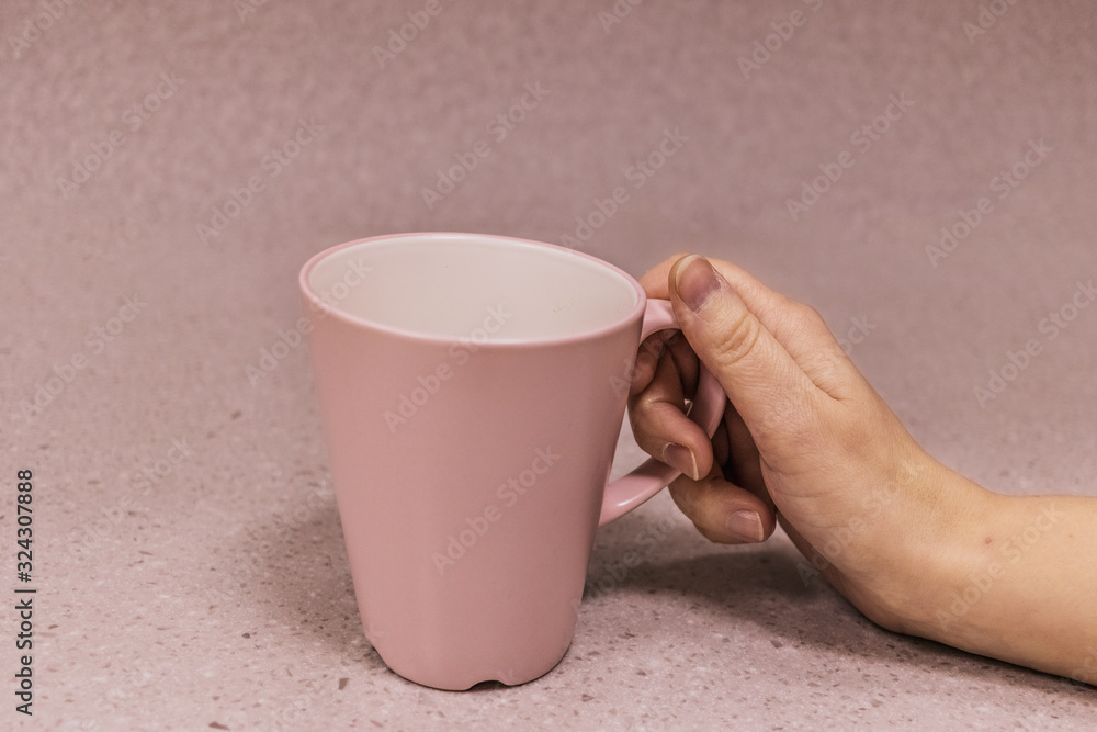 Pink cup in a female hand on a pink background Pink cup in a female hand on a pink background