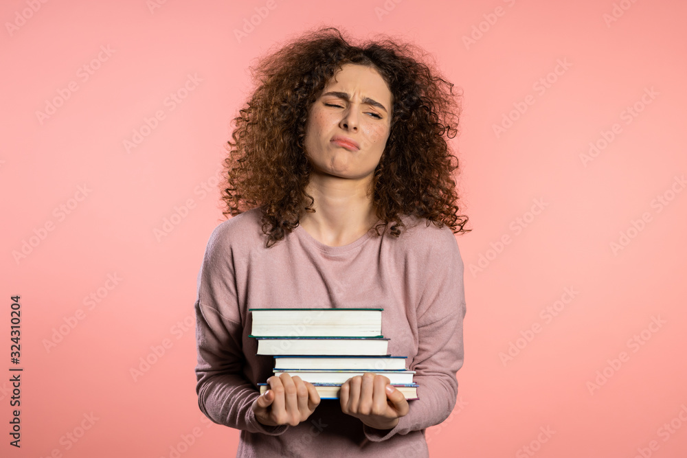 Cute female student is dissatisfied with amount of homework and books. Girl with books, she is annoyed, discouraged frustrated by studies. Cute female student is dissatisfied with amount of homework and books. Girl with books, she is annoyed, discouraged frustrated by studies.