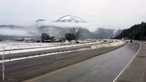 Upwards crane shot over a highway in front of a snow covered mountain with a vehicle cutting through the scene