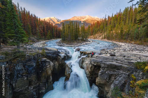 Sunwapta Falls with traveler sitting on rock in autumn forest at sunset