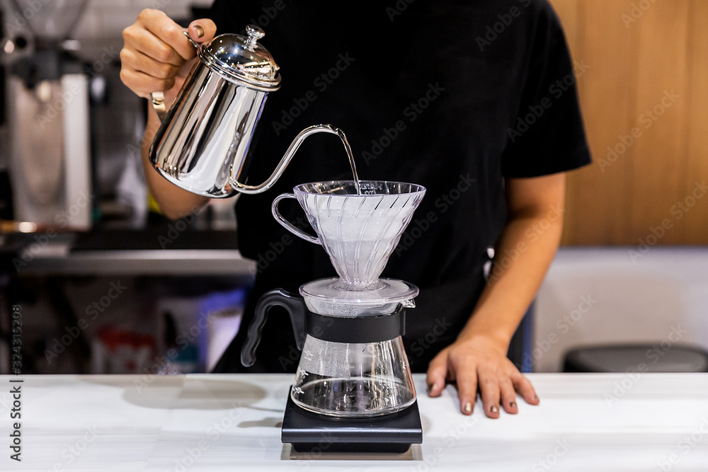 Woman barista making pour-over coffee with alternative method called Dripping. Coffee grinder, coffee stand and pour-over on marble top counter.