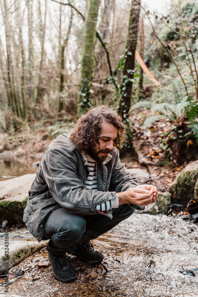 Young man crouching at stream in forest, drinking water from cupped hands Young man crouching at stream in forest, drinking water from cupped hands