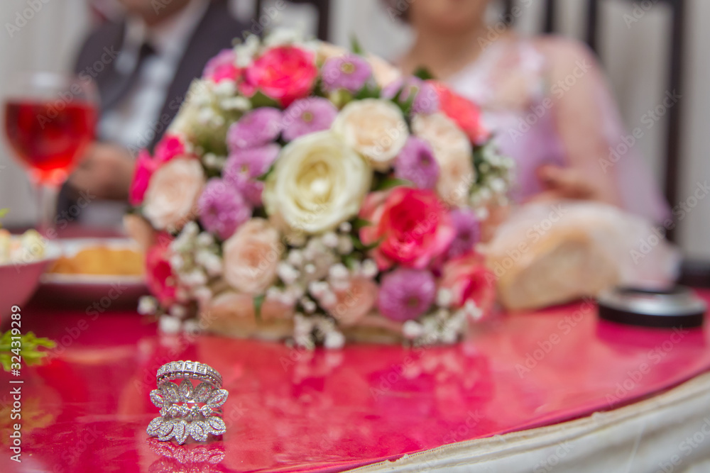 Bride and groom with Engagement gold rings put on the table, and next to them lies a wedding bouquet .red table . Wedding rings next to a flower bouquet selective focuse . Colorfull Wedding flowers .