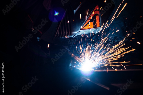 A masked welder in full darkness welds a metal.