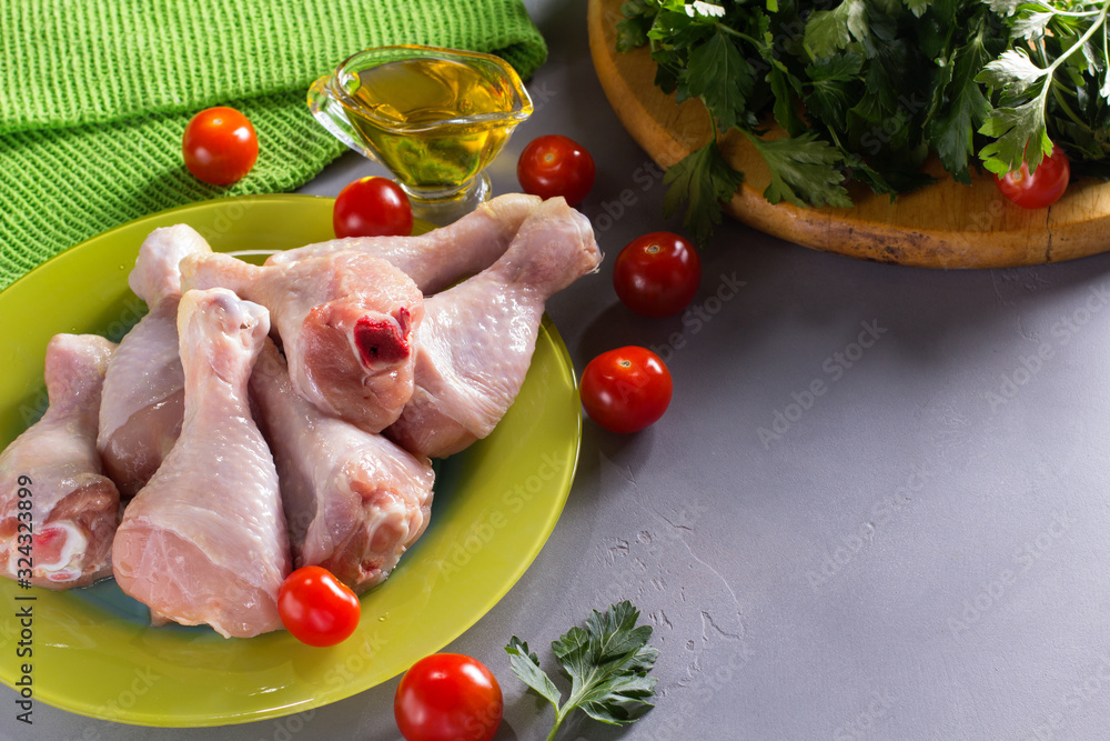 Raw chicken legs with parsley and tomatoes on grey background.