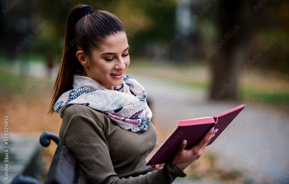 Obraz premium Young woman sitting in the park and reading a book. Lifestyle, education concept