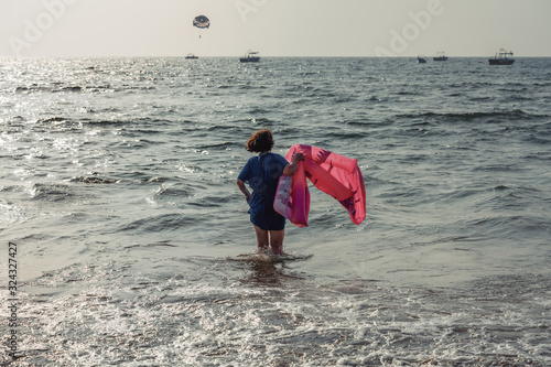 A woman stands with an air mattress on a sandy seashore on a sunny warm summer day. Tourism and leisure concept