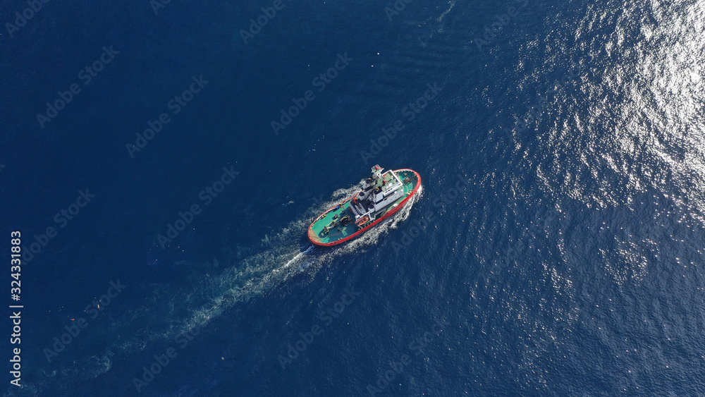 Naklejka premium Aerial drone photo of tug assisting boat cruising near commercial container area of Perama, Attica, Greece