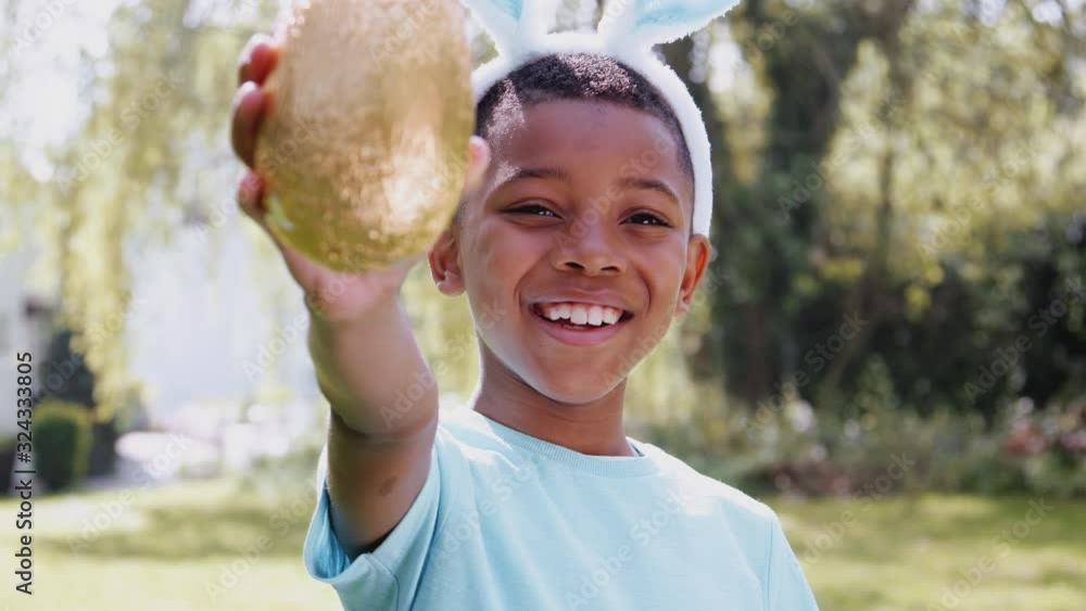 Portrait Of Boy Wearing Bunny Ears Holding Chocolate Egg On Easter Egg Hunt In Garden Portrait Of Boy Wearing Bunny Ears Holding Chocolate Egg On Easter Egg Hunt In Garden