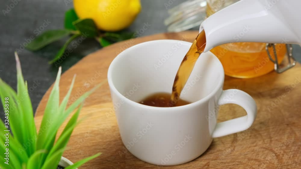 Pour tea in white cup on wooden board. Close up. Pour tea in white cup on wooden board. Close up.