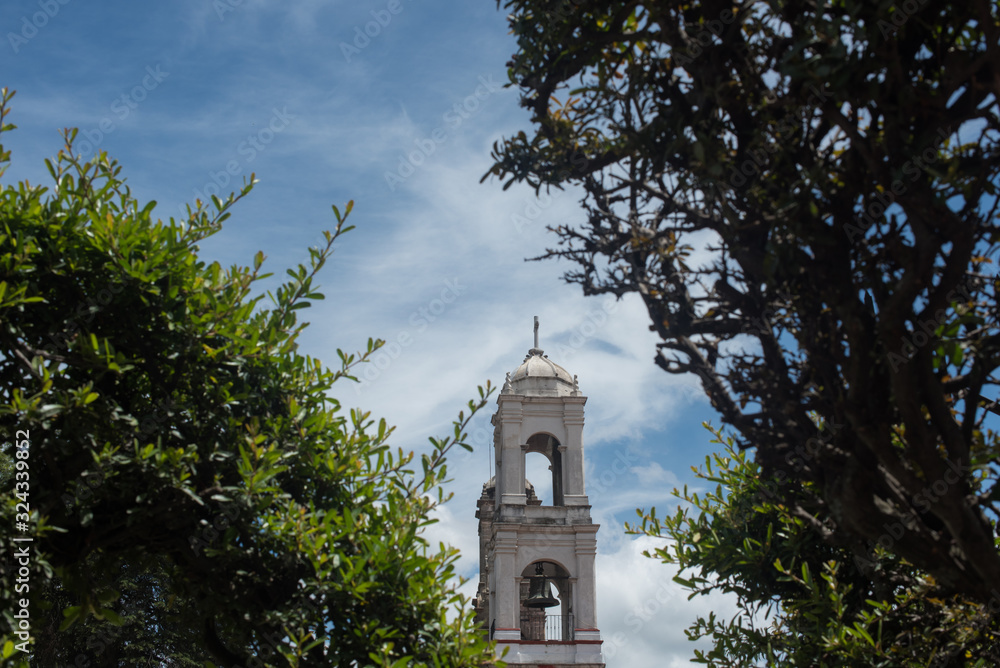 Tower of the cathedral of Villa del carbon  between green foliage 