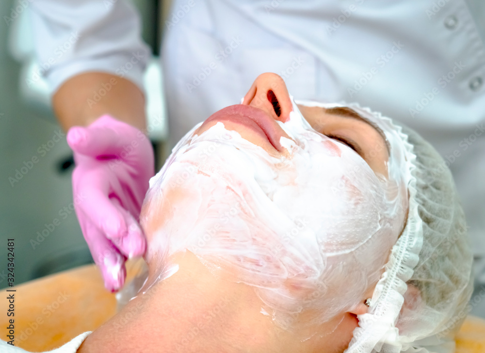 Girl beautician applies a to rejuvenate a mask on the face of an attractive girl in a spa salon. Beautiful woman during rejuvenation procedure. Face treatment at cosmetic clinic. Girl beautician applies a to rejuvenate a mask on the face of an attractive girl in a spa salon. Beautiful woman during rejuvenation procedure. Face treatment at cosmetic clinic.