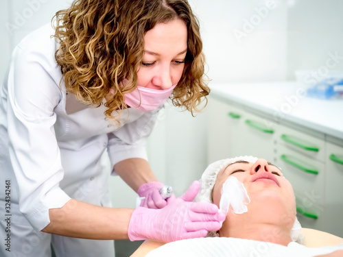 Girl beautician applies a to rejuvenate a mask on the face of an attractive girl in a spa salon. The concept of self-care and rejuvenation. Beautiful woman during rejuvenation procedure.