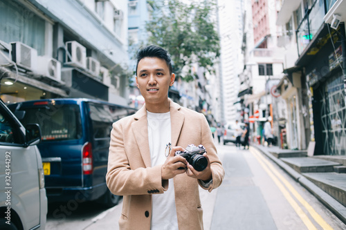 Ethnic young man holding photo camera on city street