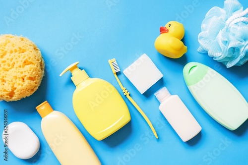 Yellow sponge, soap bar, shampoo bottle, toothbrush, shower gel, hair balm and rubber duck on a blue background. Flat lay photography bath products, baby care cosmetic
