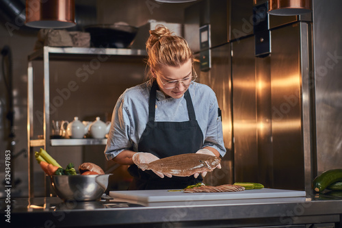 Photography Beautiful and stylish woman chef standing in a dark restaurant kitchen next to c