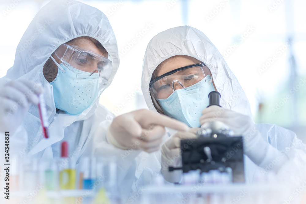 A female scientist wearing a mask and looking through the microscope in the laboratory, Concept, The scientists wear white protective clothing is experimenting with drug anti- Coronavirus A female scientist wearing a mask and looking through the microscope in the laboratory, Concept, The scientists wear white protective clothing is experimenting with drug anti- Coronavirus